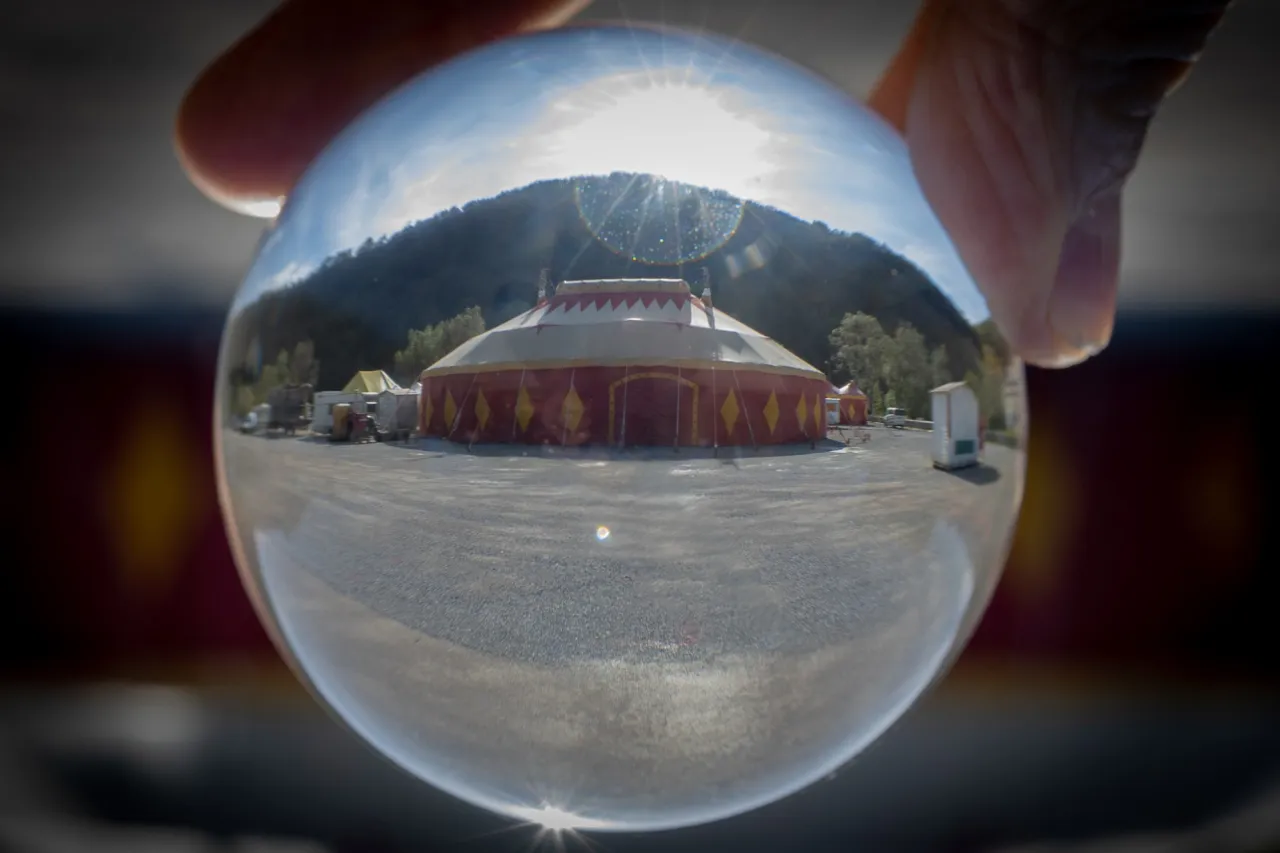 Le chapiteau rouge et jaune du festival, vu à l'envers à travers une boule de cristal tenue à bout de bras